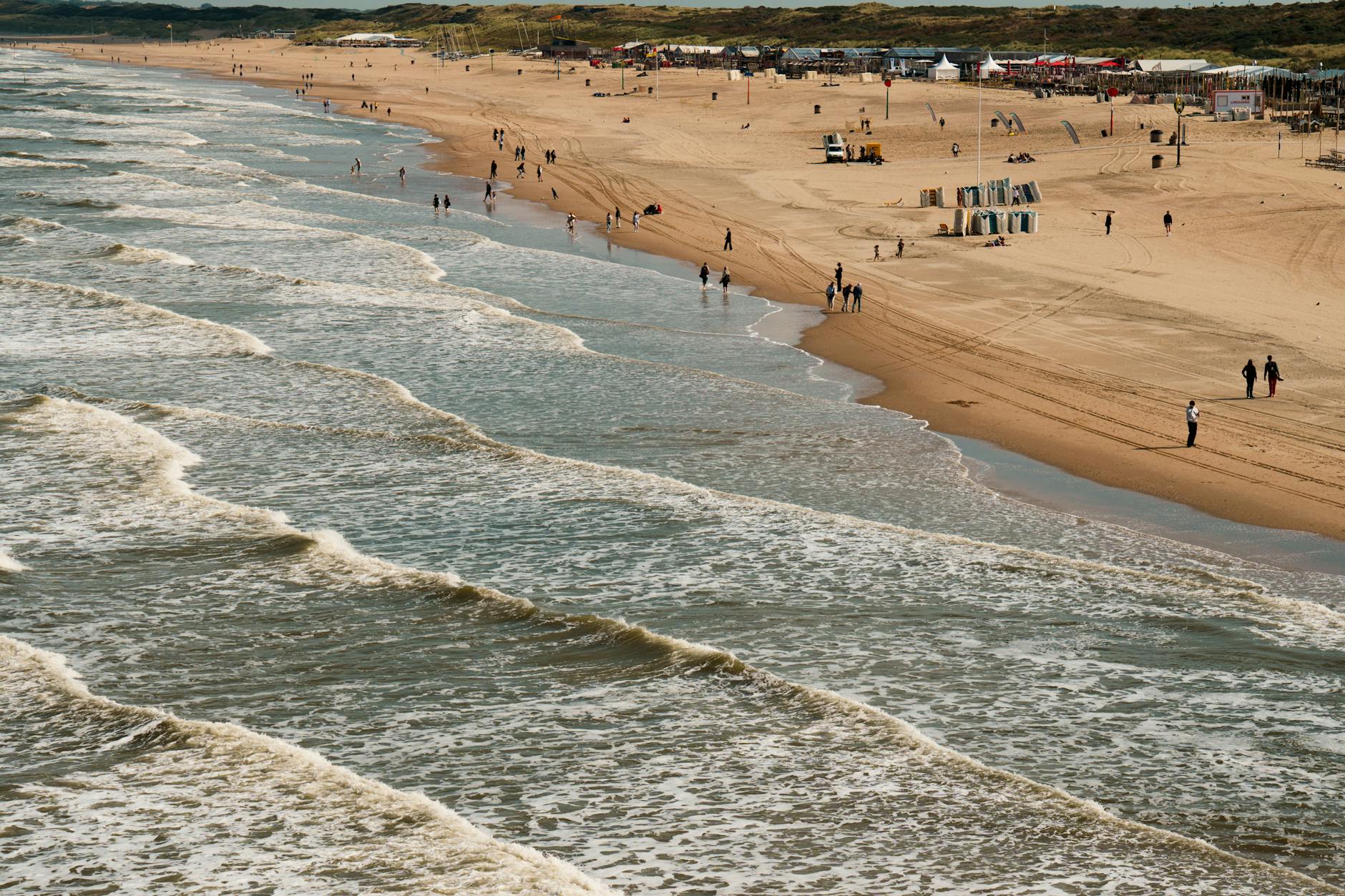 Plażowicze spacerują przy falach na plaży Scheveningen w Holandii